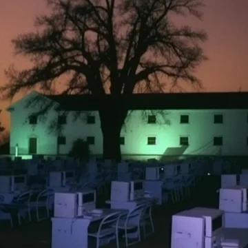 Empty chairs outside a green-lit building at dusk.