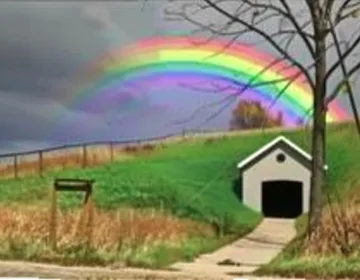Rainbow above a small house and grassy field.
