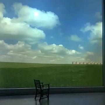 Lone chair facing a green field and clouds.