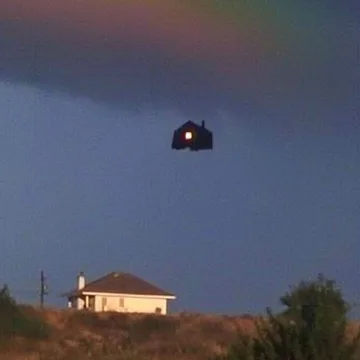 Small floating house above a neighborhood at dusk.