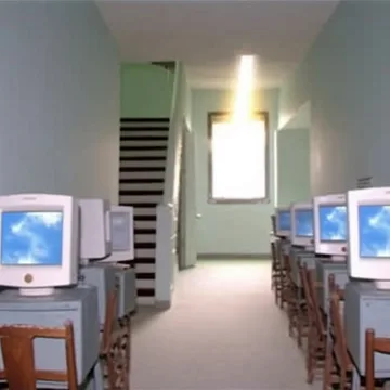Old computers beside a staircase and bright window.