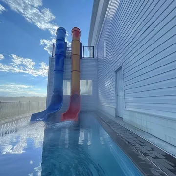 Tall blue slide above a pool beside a white building.