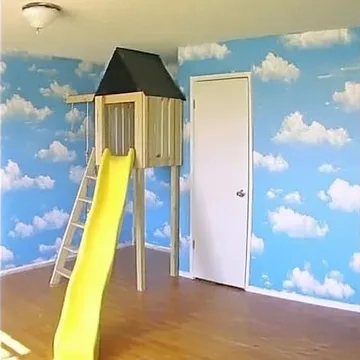 Yellow playground slide beside a cloud-painted wall.