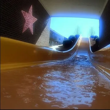 Water flowing down a slide toward a bright opening.