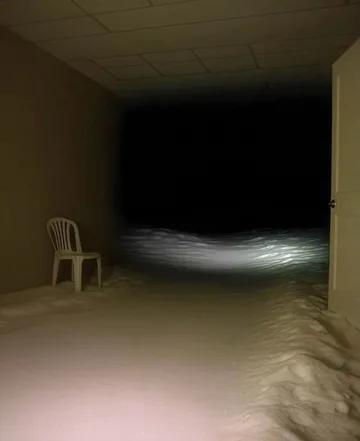 Lone chair facing a dark opening in a room.