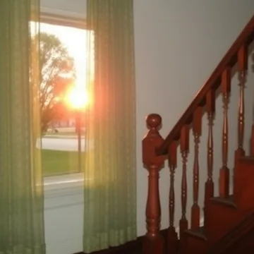 Sunset through a door beside a wooden staircase.