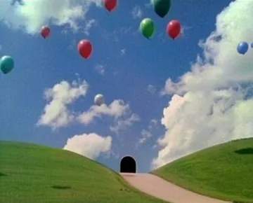 Balloons above a winding path through green hills.