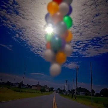 Balloons above an empty road under a textured sky.