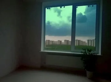 Window overlooking a house under green clouds.