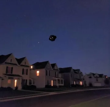 Small floating house above a neighborhood at dusk.
