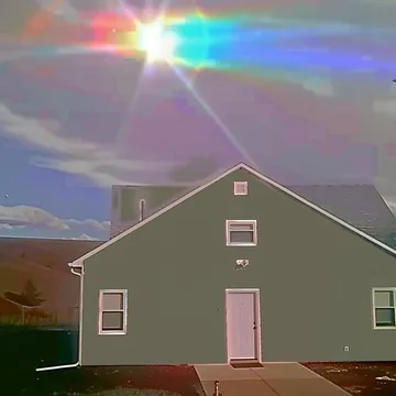Pale house beneath a rainbow flare.