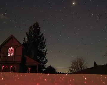 House with red windows beneath a moonlit sky.