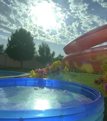 Circular pool beside a slide and sunlit trees.
