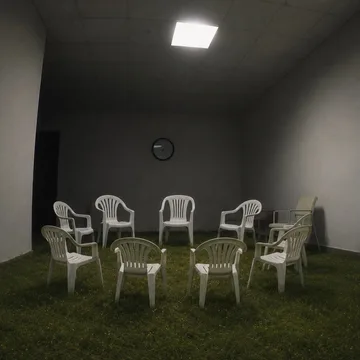 White chairs arranged on grass inside a gray room.