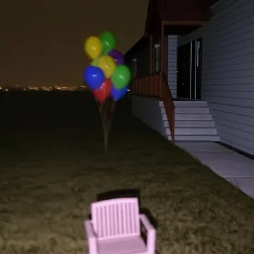 Balloons above a pink chair outside a house at night.