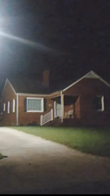 Small brick house beside an illuminated lawn at night.